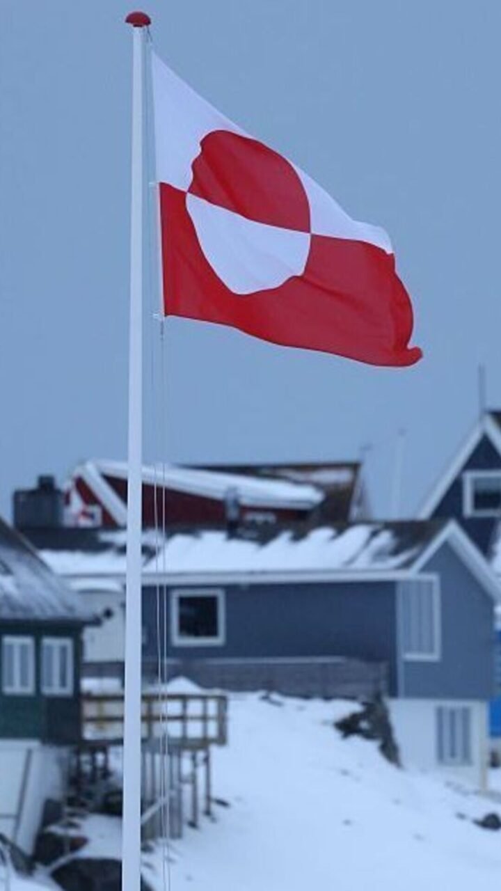 Bandeira da Groenlândia tremulando com casas nevadas ao fundo